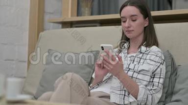 美丽的年轻<strong>女子坐在沙发上</strong>使用智能手机